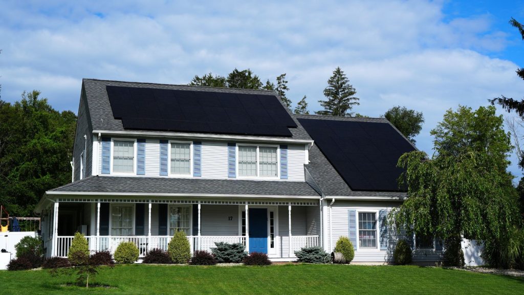Two-story New Jersey home with solar panels installed on the roof under a bright blue sky